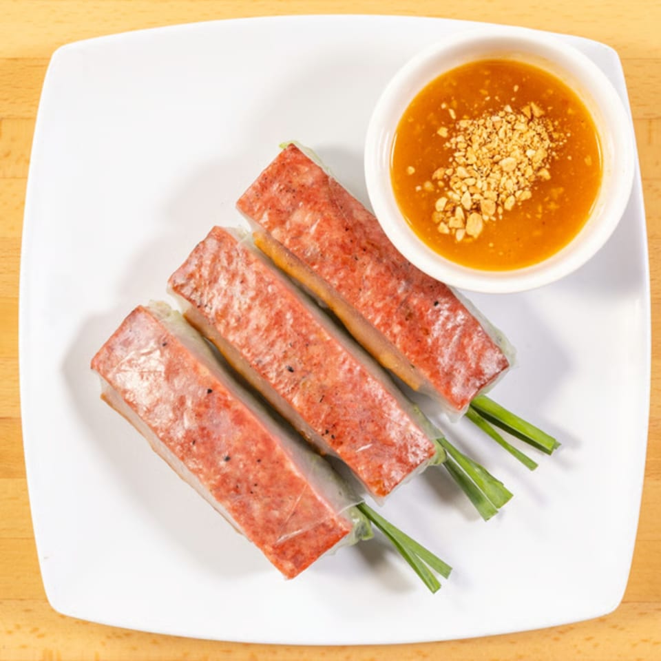 Three Vietnamese spring rolls with red meat and green chives, served with peanut dipping sauce.