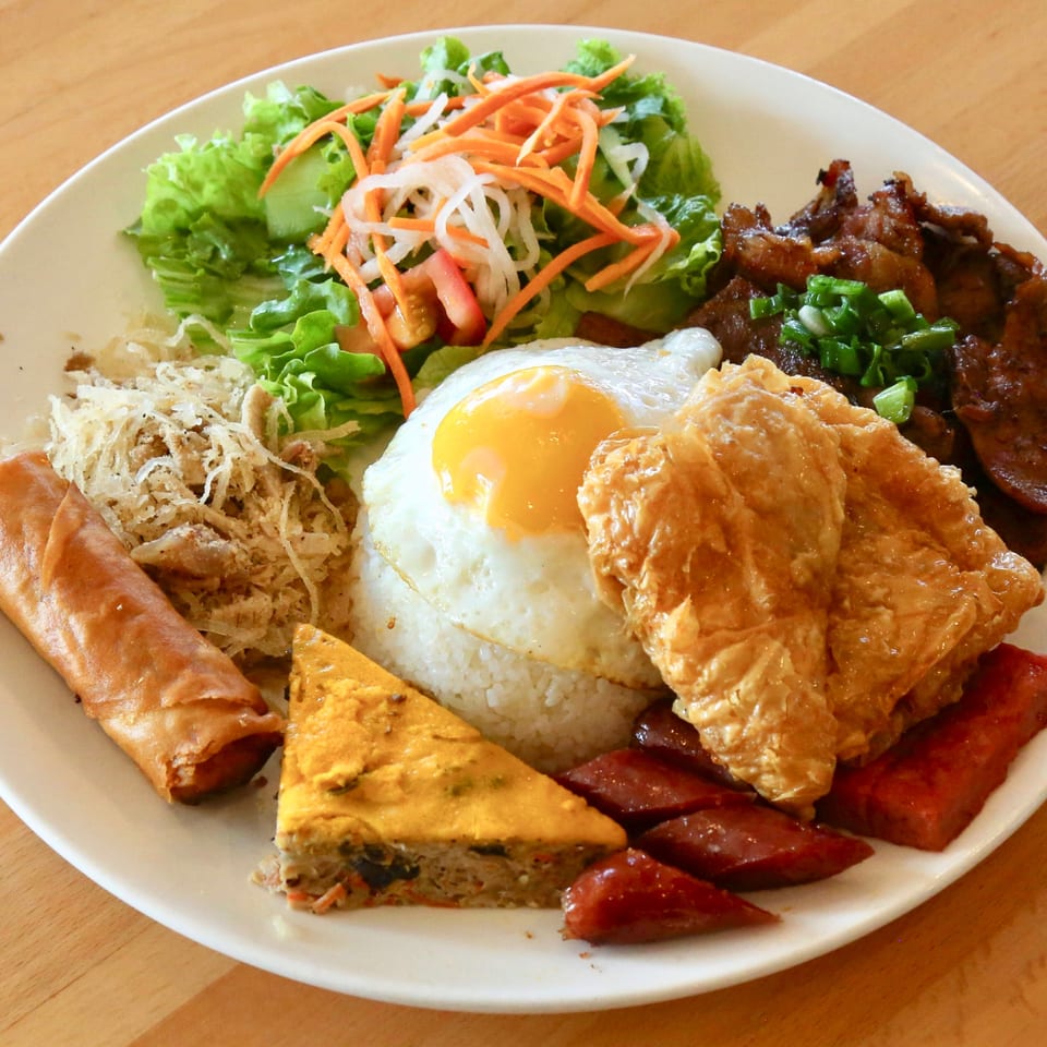 A Vietnamese combination plate with rice, fried egg, spring roll, grilled meats, and salad.