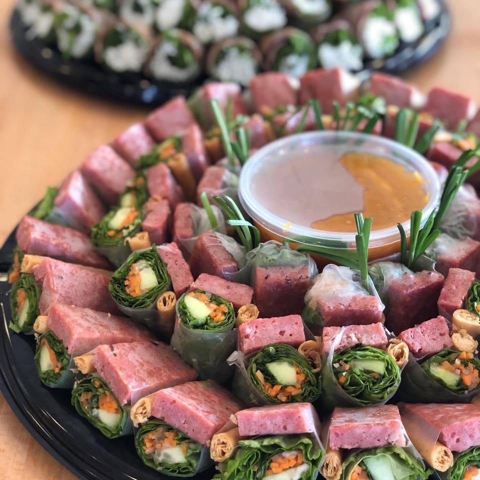 A platter of Vietnamese spring rolls with pink ham, vegetables, and a dipping sauce.