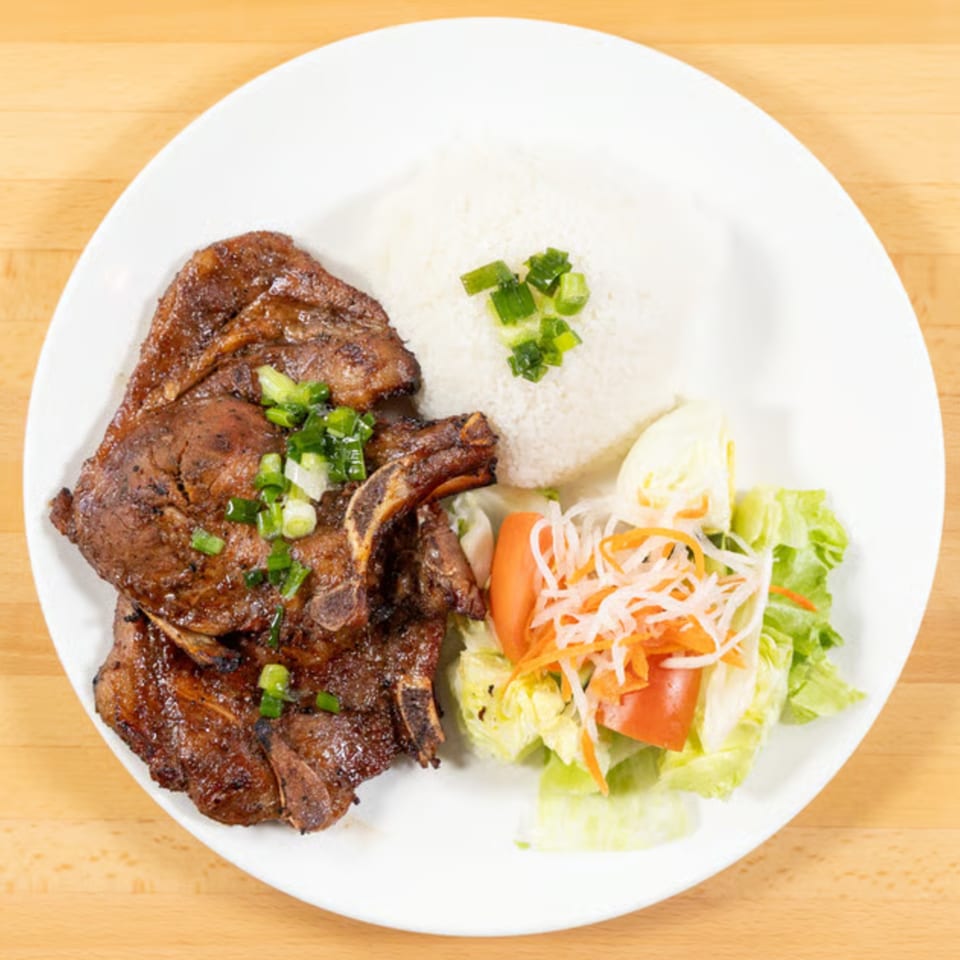 Vietnamese grilled pork chops with rice, topped with green onions, and a side salad.