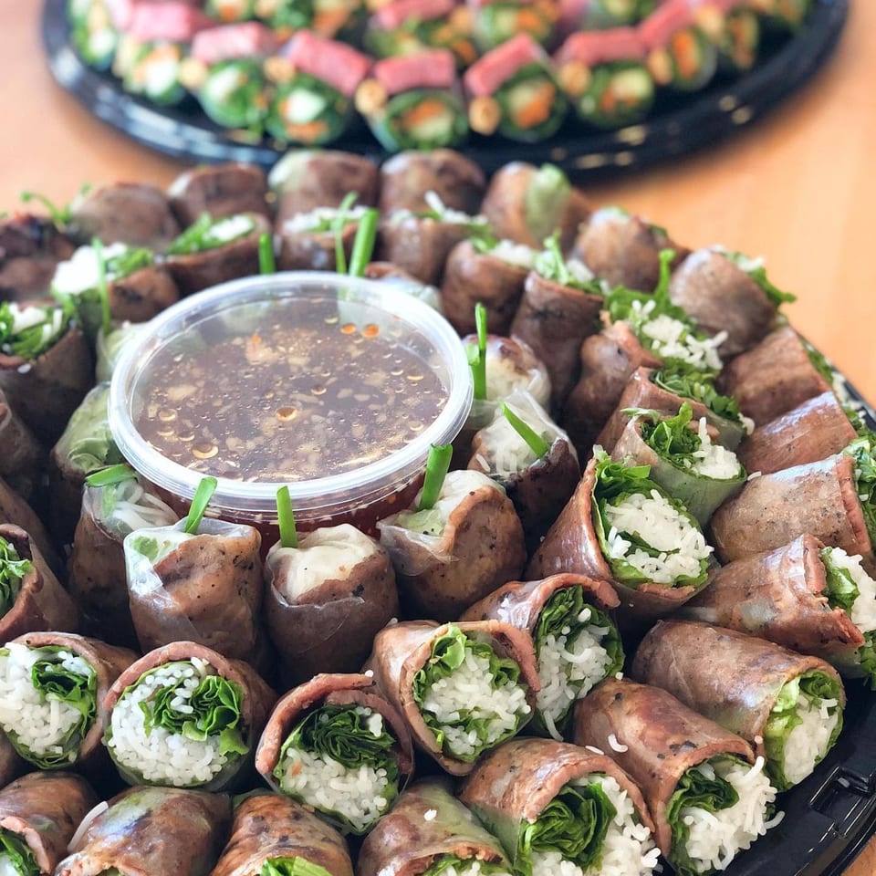 Platter of fresh spring rolls with rice, lettuce, and meat, served with a dipping sauce.