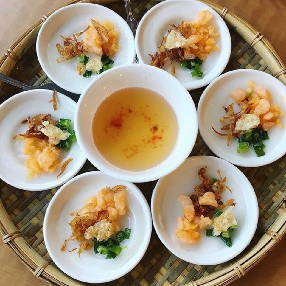 A bamboo tray holds six small white dishes of Vietnamese Bánh Bèo, with a central dipping sauce.